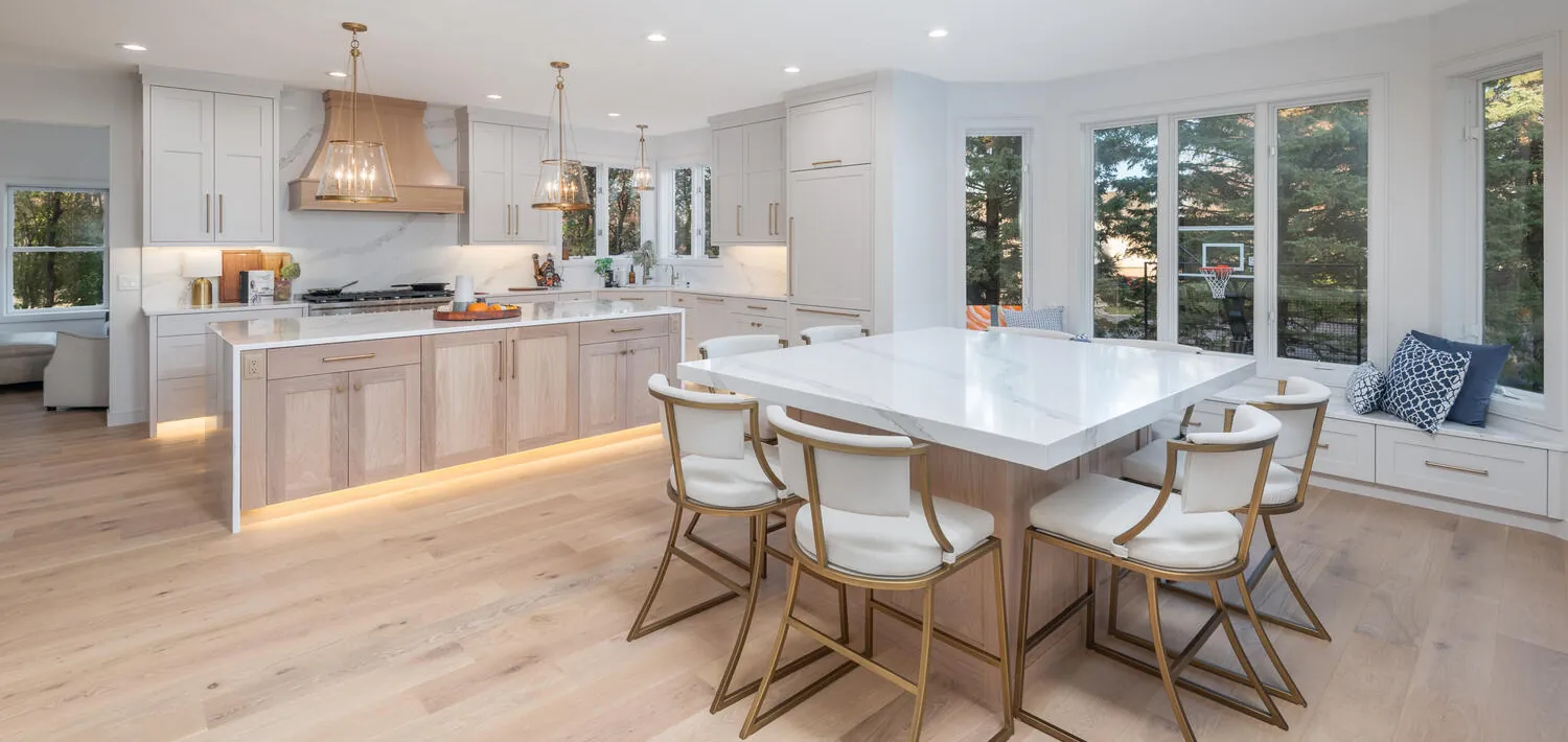 Light white oak hardwood floor in an open kitchen with a waterfall island and gold-frame chairs, installed by Anton's Floorcovering in Bloomington, MN