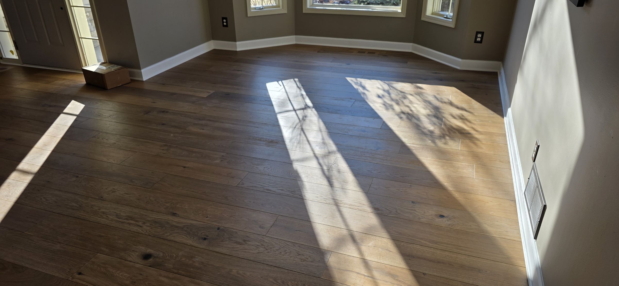 Wide-plank hardwood in a sunlit living room with a bay window, installed by Anton's Floorcovering