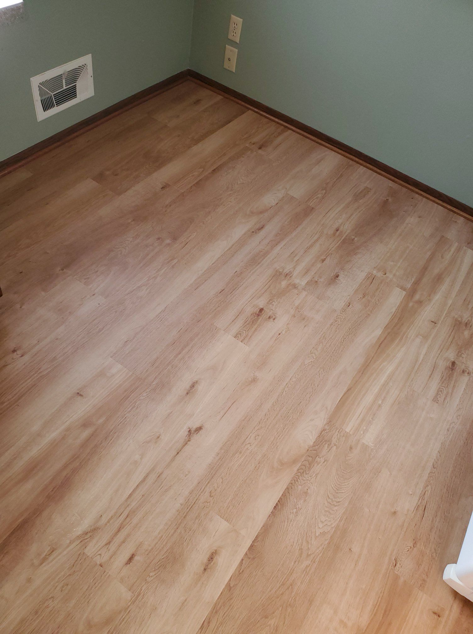 Light tan plank LVP flooring installed in a bedroom with green walls.