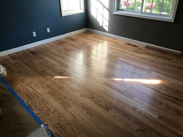 Newly installed red oak hardwood flooring in a bedroom with dark walls and windows.