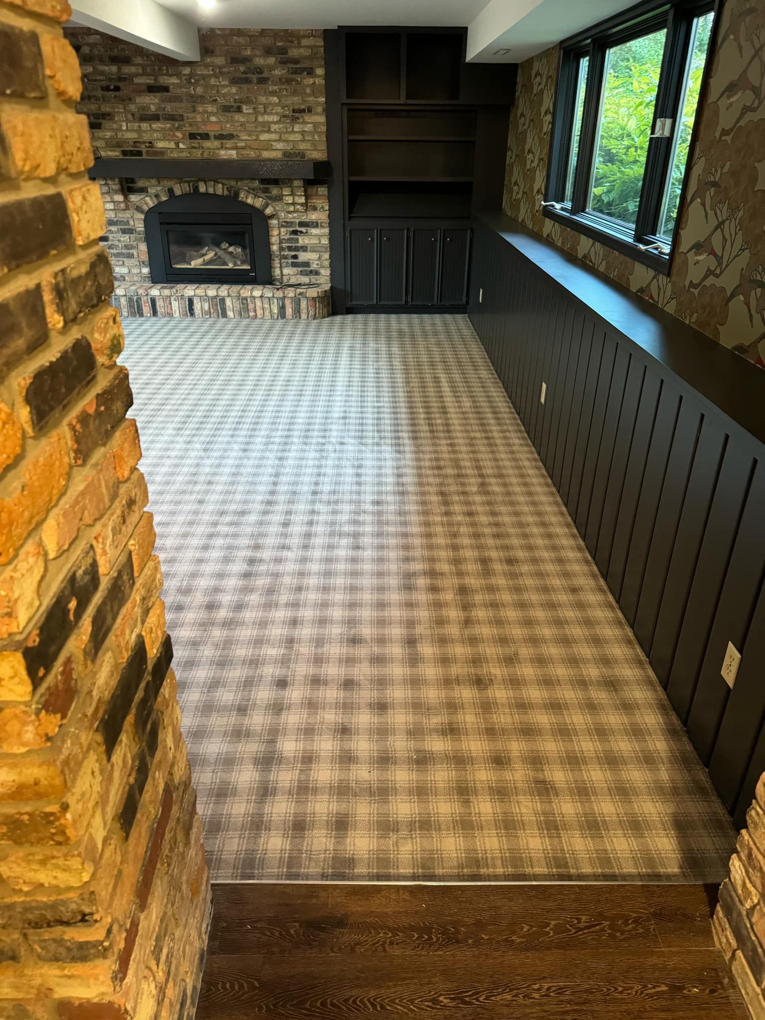 Sunroom with installed gray plaid carpet, brick fireplace, and dark wood wainscoting.