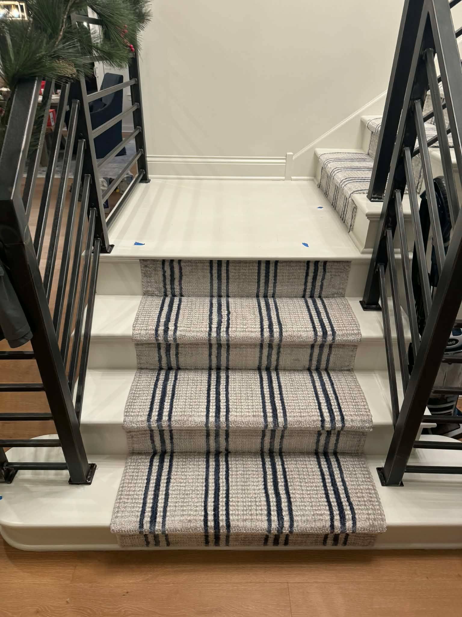 Carpet-covered staircase with gray and beige striped runner and black metal railings on both sides.