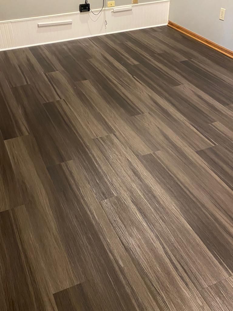 Gray and brown wood-grain luxury vinyl plank flooring installed in a basement room with white walls and baseboard trim.