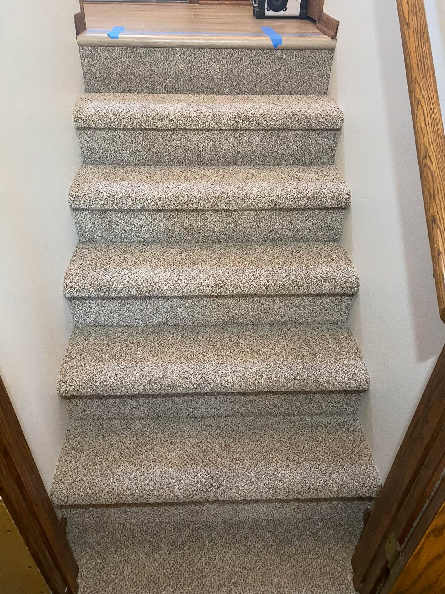 Gray and tan textured carpet installed on interior staircase with wood railings.