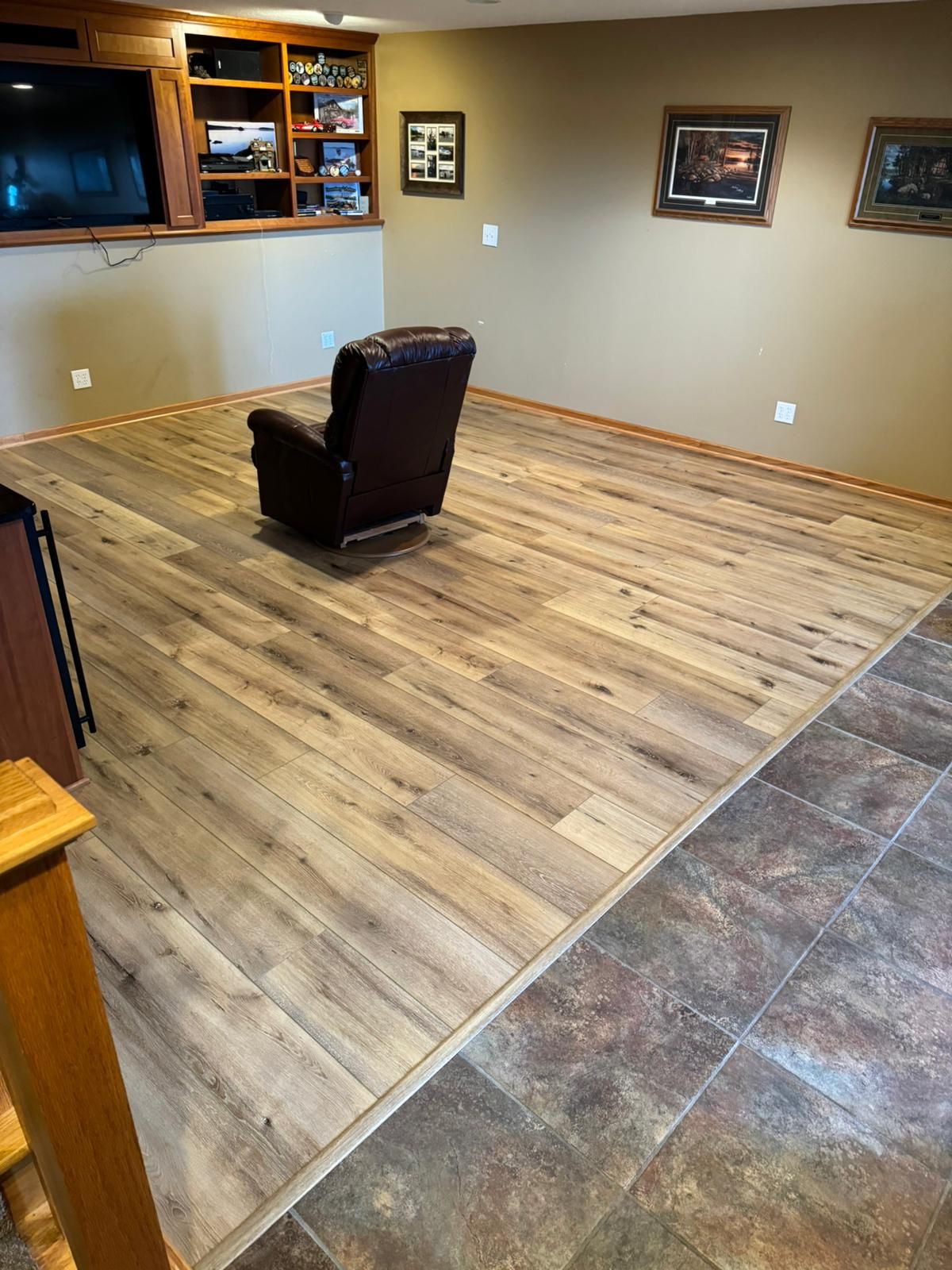 Basement recreation room with light tan wood-look plank flooring and a dark leather recliner.