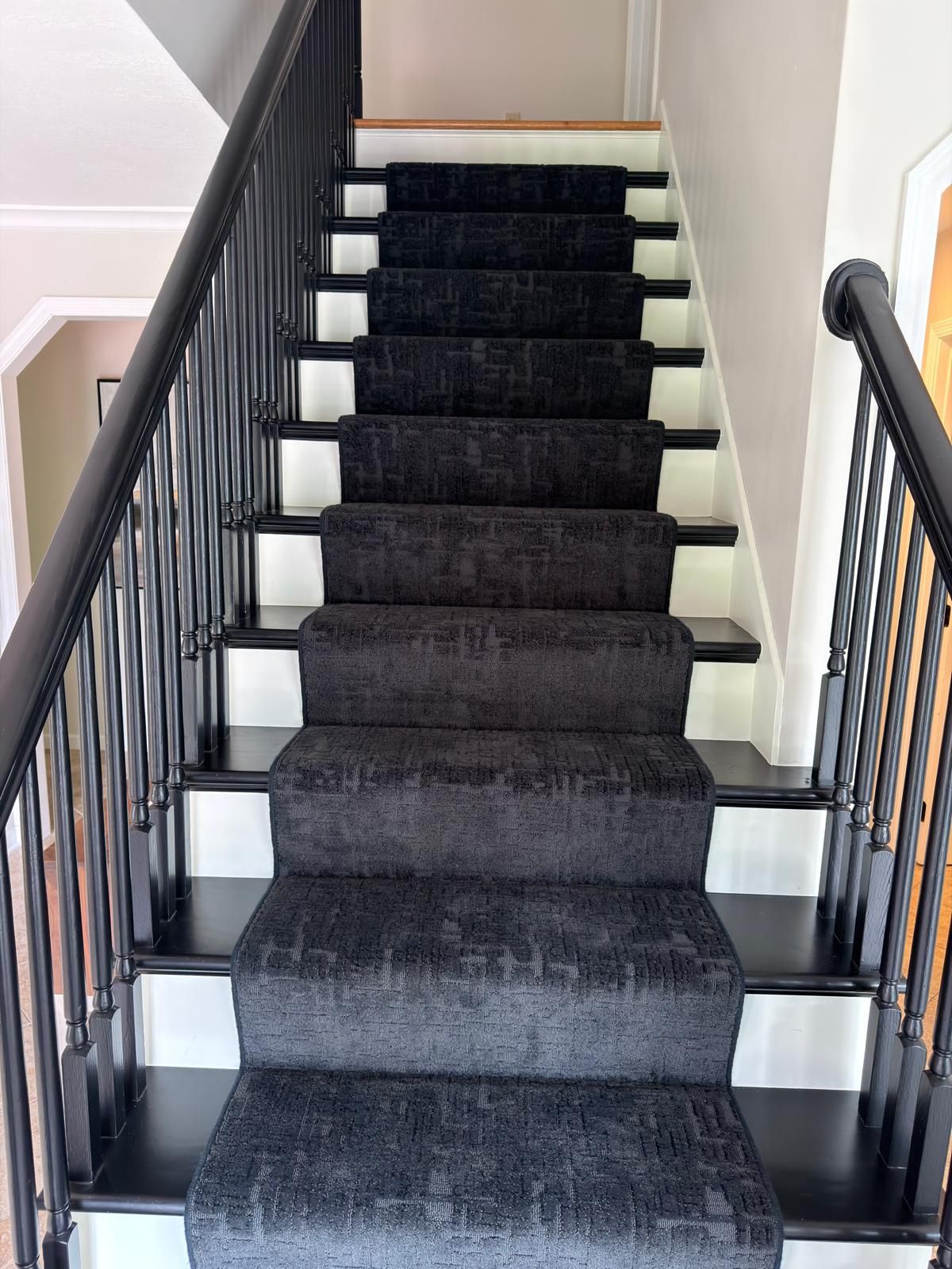 Dark carpet stair runners installed on white painted stairs with black metal railings.