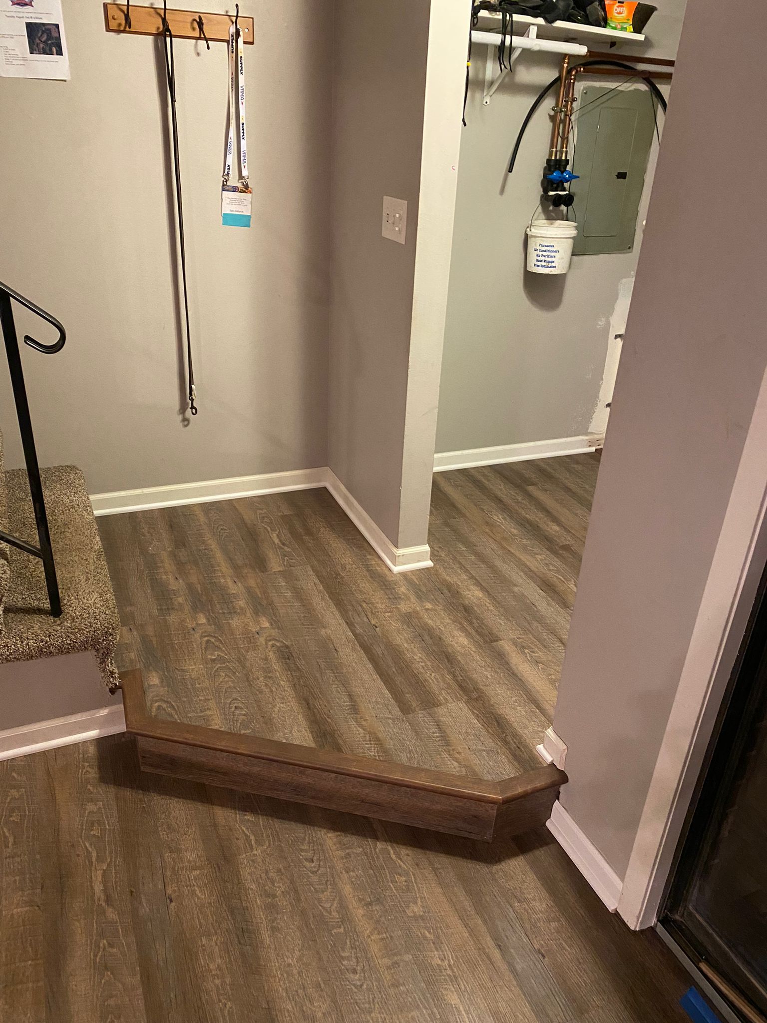 Basement hallway with medium brown wood-look LVP flooring and white baseboards installed around door frames and walls.