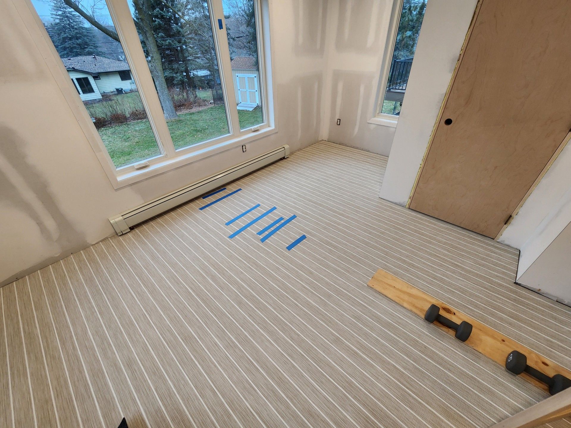 Light gray luxury vinyl plank flooring being installed in a living room with large windows.