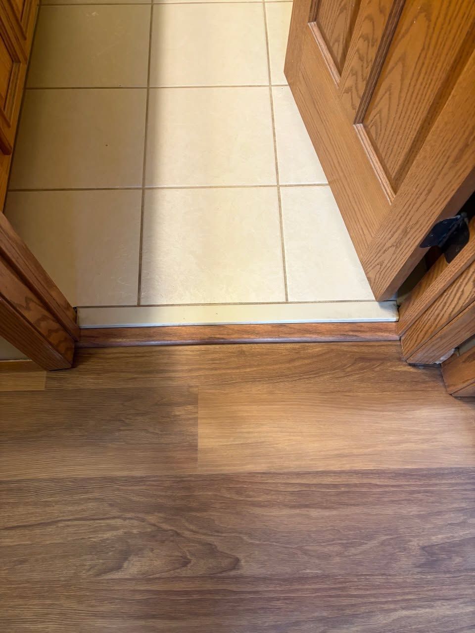 Entry flooring with light tan tile transitioning to medium brown wood-look LVP planks with wood grain detail.
