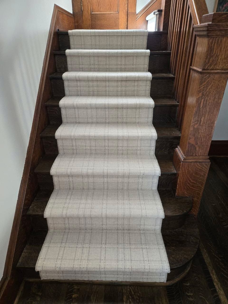 Light beige textured carpet runner installed on dark wood stairs with contrasting dark binding on edges.
