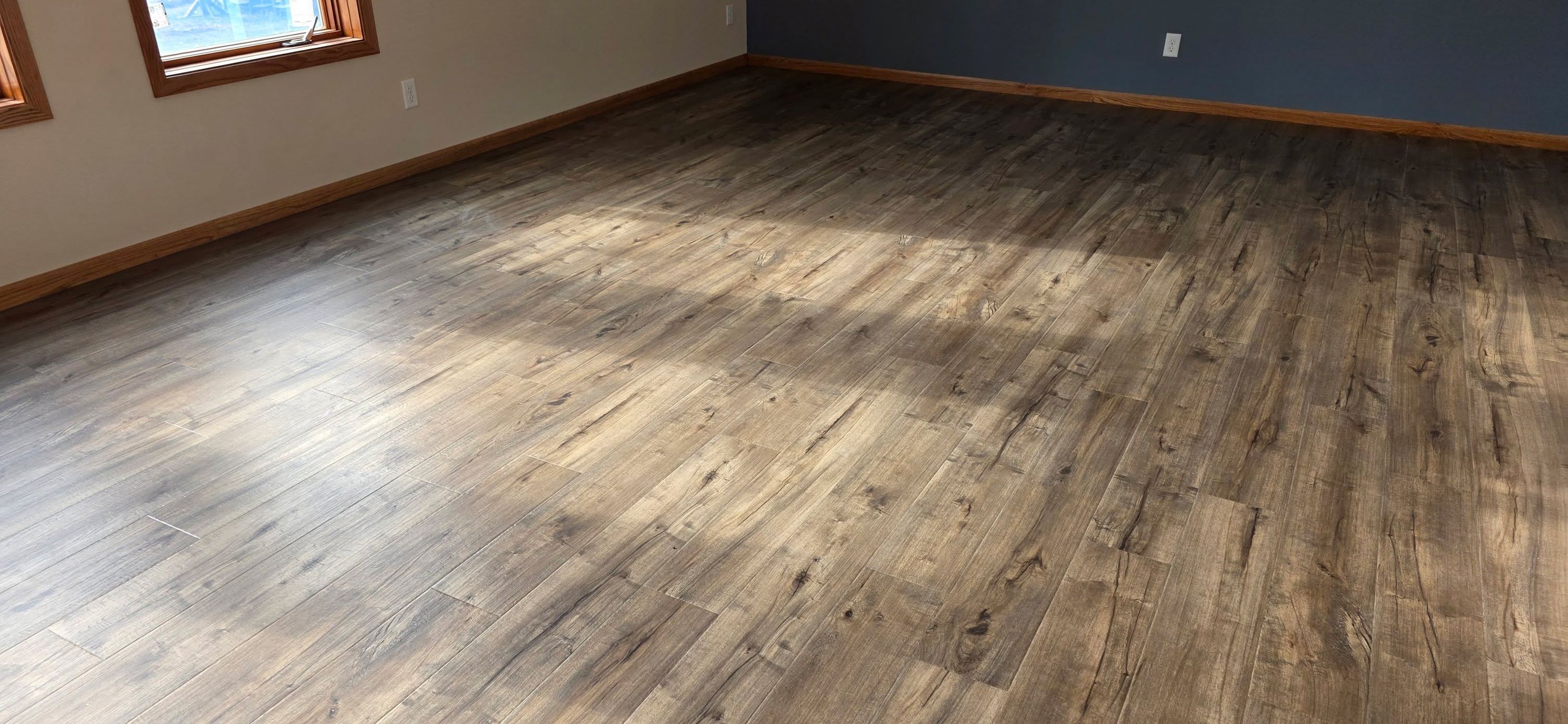 Luxury vinyl plank flooring in medium brown tones installed in a bedroom with wood grain texture and matte finish.