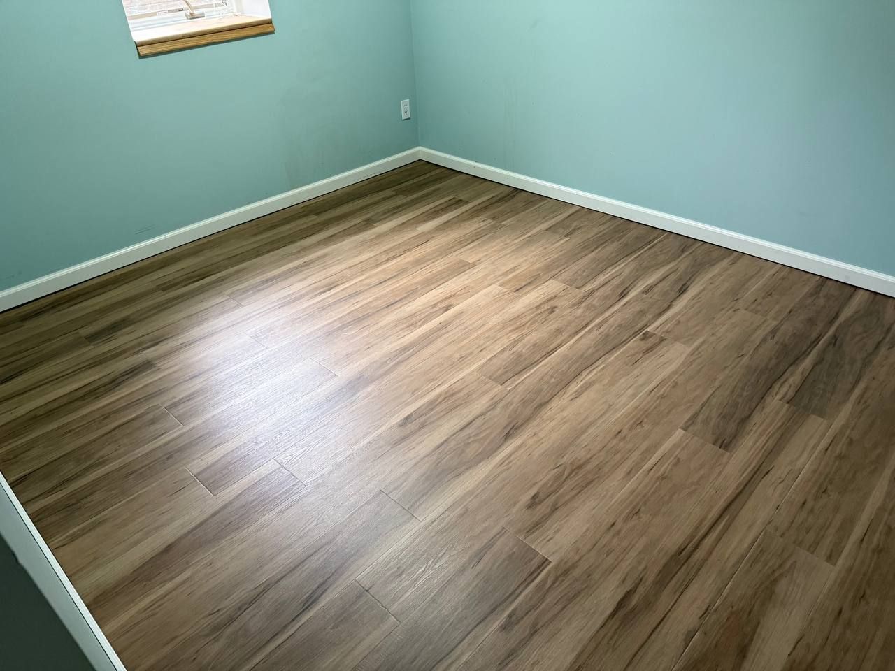 Newly installed medium brown wood-look LVP planks in a bedroom with white baseboards and turquoise walls.