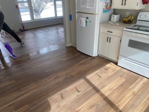 Kitchen with newly installed medium brown wood-look LVP flooring next to white appliances.
