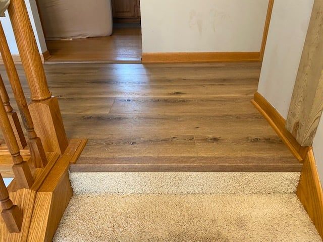 Wood-look LVP plank flooring on stairs transitioning to carpeted landing with wood baseboards and railings.