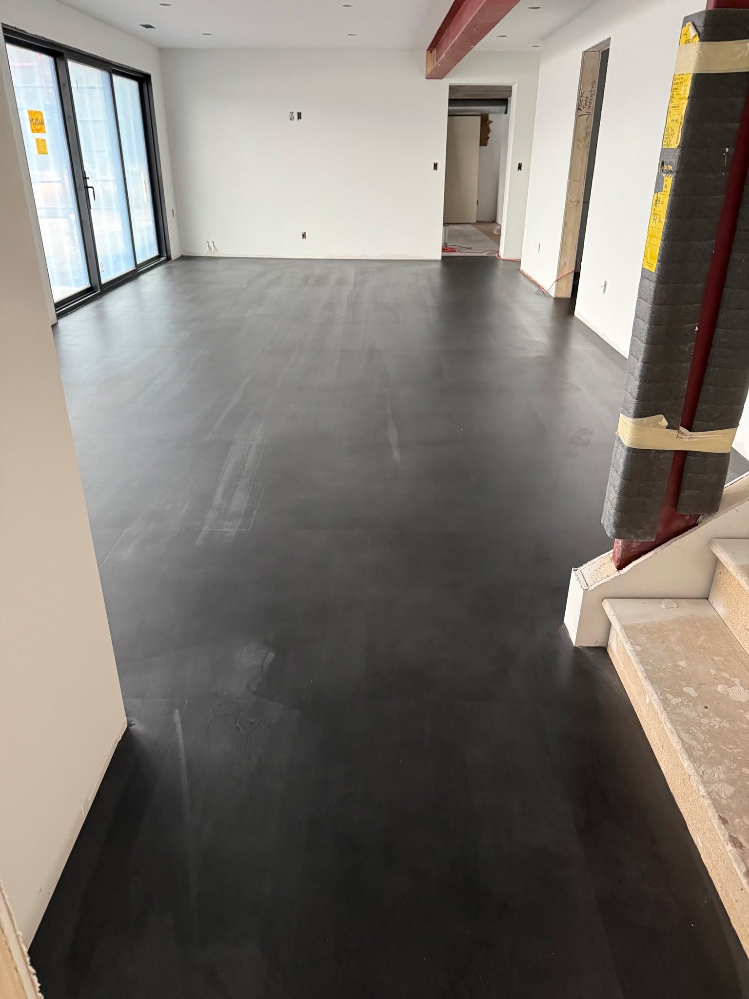 New dark gray luxury vinyl plank flooring installed in an empty commercial or residential space with white walls and support columns.