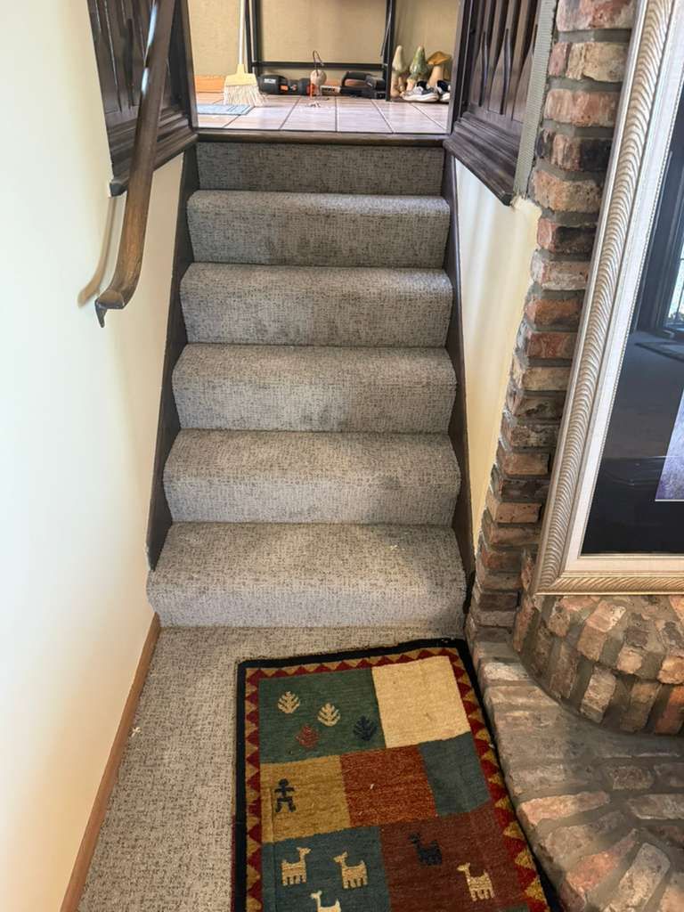Gray textured carpet installed on residential staircase with brick walls visible on right side.