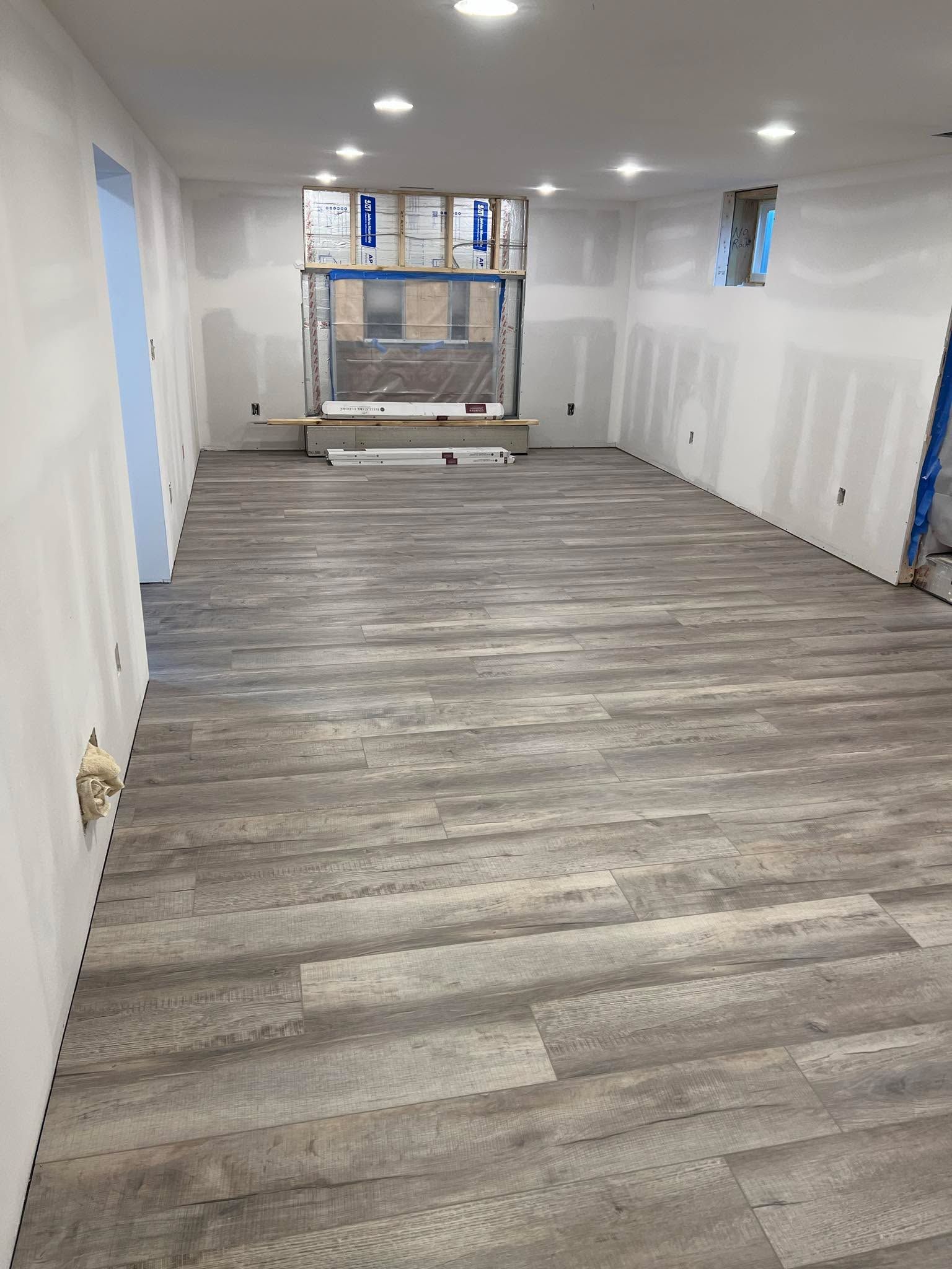 Newly installed gray and brown luxury vinyl plank flooring in a basement with white drywall and recessed lighting.
