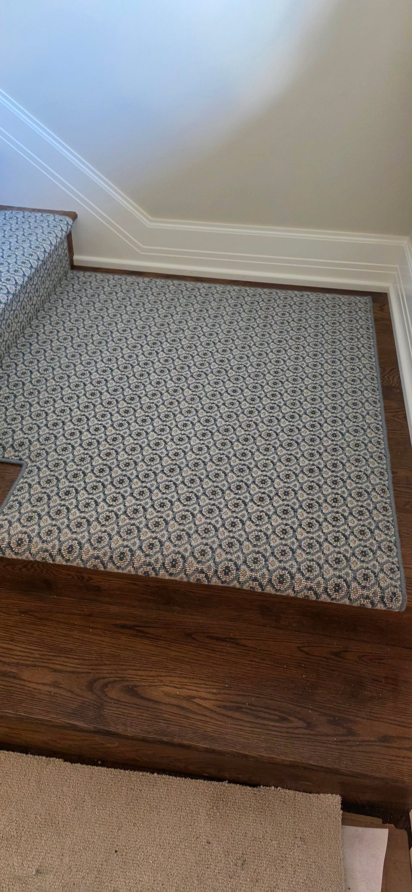 Gray and cream patterned carpet installed in a bedroom with wood trim border and transition to hardwood flooring.