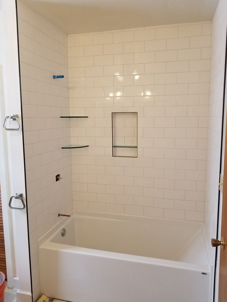 White subway tile tub surround with glass shower enclosure and built-in shelving.