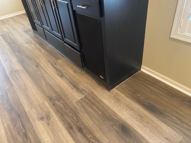 LVP plank flooring in warm brown tones installed in kitchen with black cabinetry.