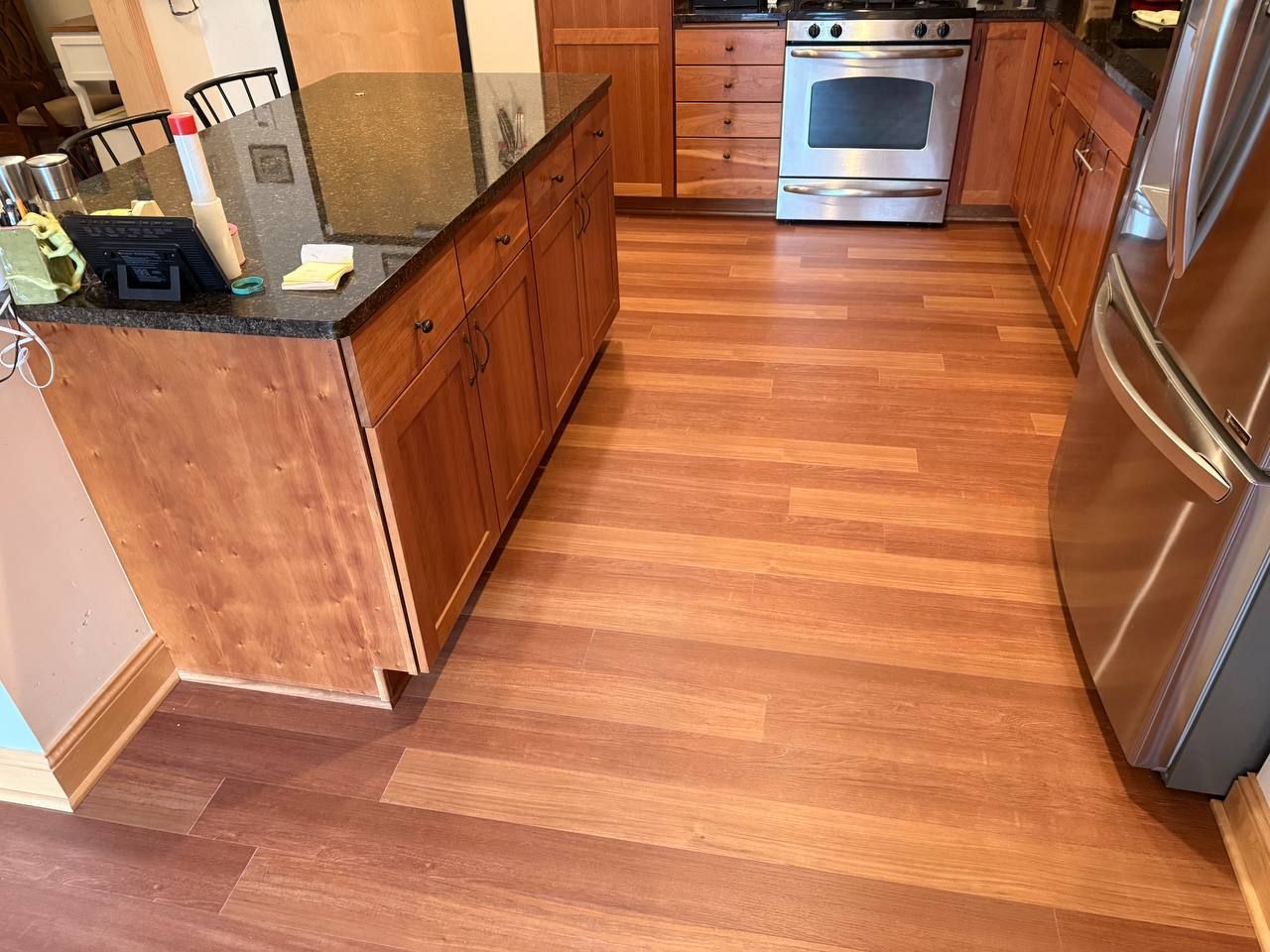 Kitchen with medium brown plank LVP flooring, wooden cabinetry, island, and stainless steel appliances.
