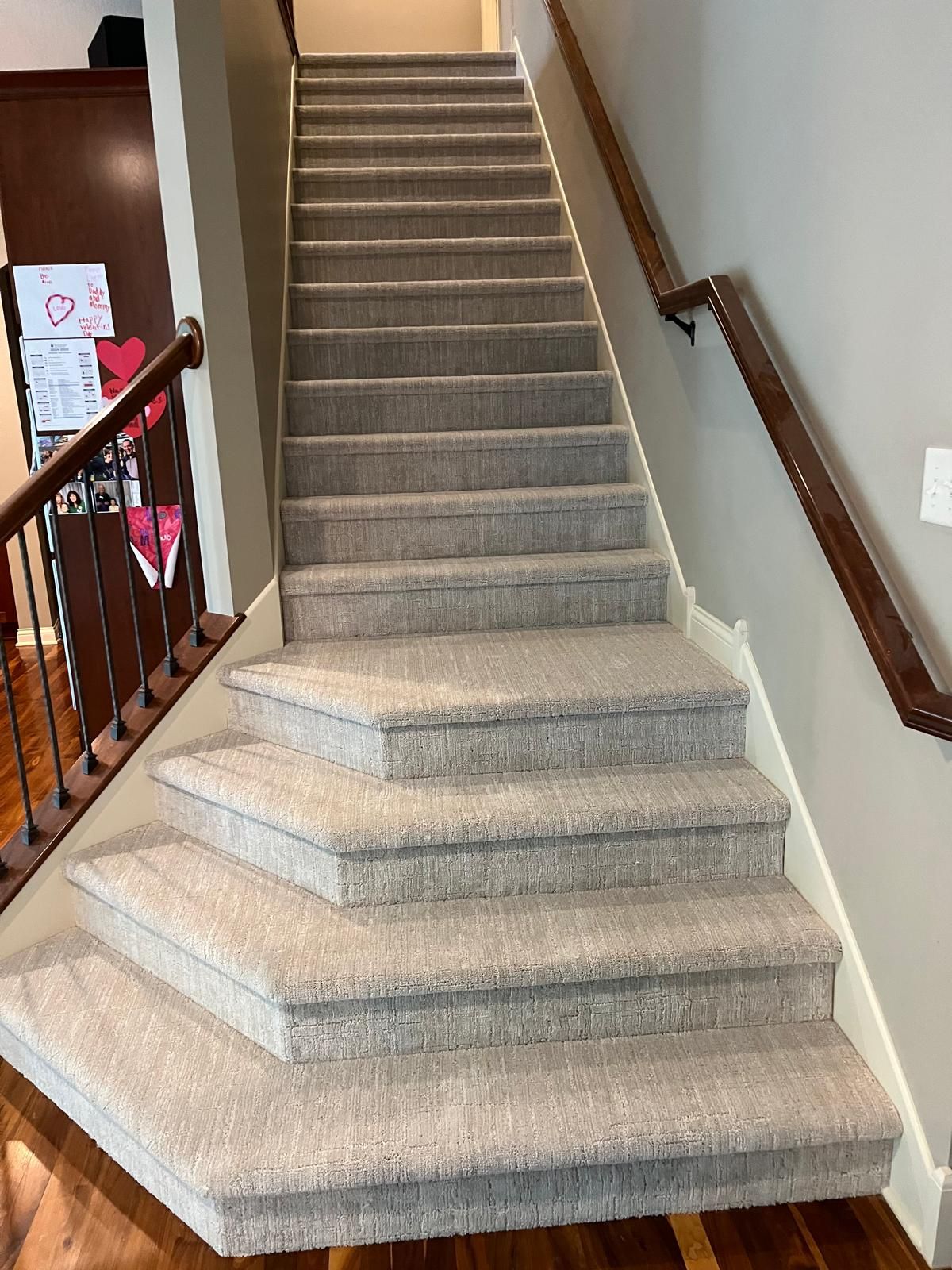 Carpeted staircase with gray and beige tones and wooden railings in a residential home.