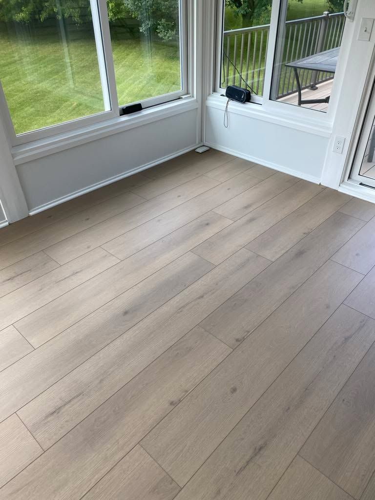 Click-together LVP plank flooring in light tan and gray tones installed in a room with large windows and glass doors overlooking a deck and yard.