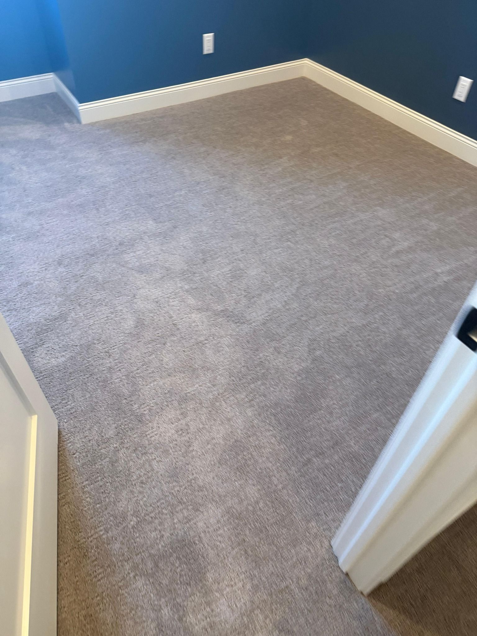 Gray carpet installed in a bedroom with blue walls and white baseboards.