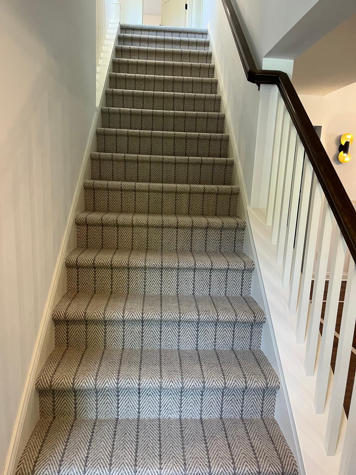 Carpet with chevron pattern installed on staircase with dark handrail and white walls.