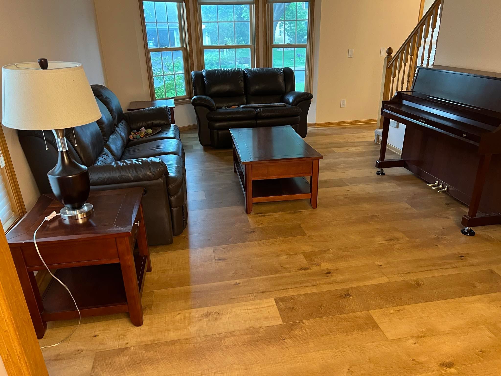 Living room with wide plank LVP flooring in medium brown tones, black leather furniture, and piano.