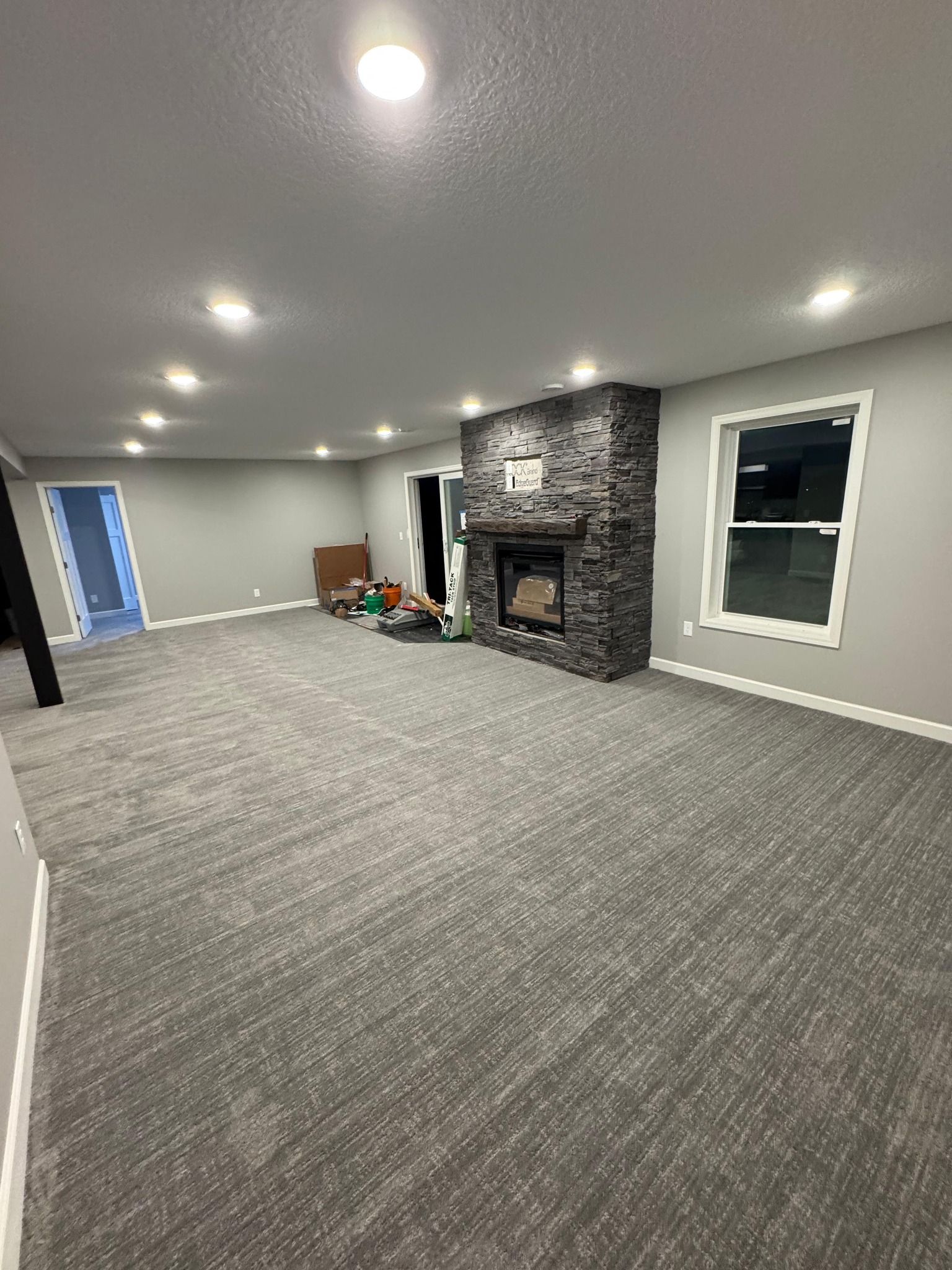 Finished basement with new gray carpet, fireplace with stone surround, and recessed ceiling lights.
