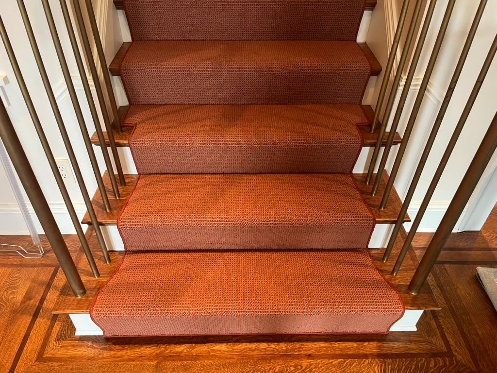 Carpeted staircase with orange-brown runner and metal spindles overlooking hardwood landing.