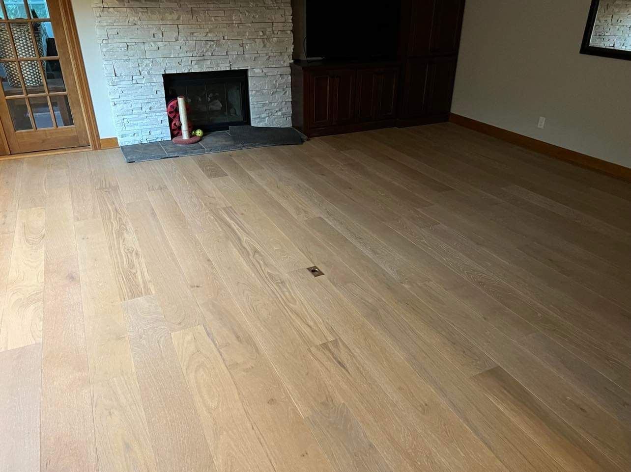 Light tan and gray hardwood plank flooring in a living room with a fireplace and white brick chimney.