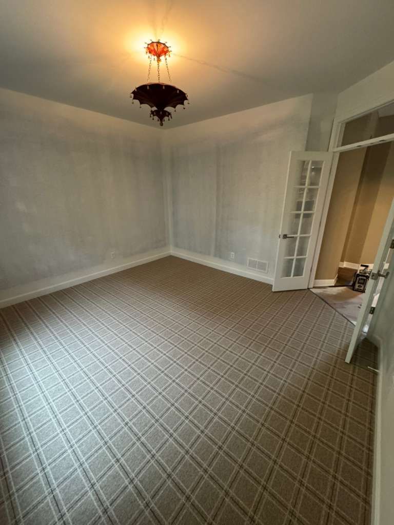 Newly installed beige and gray geometric patterned carpet in an empty office room with white walls.