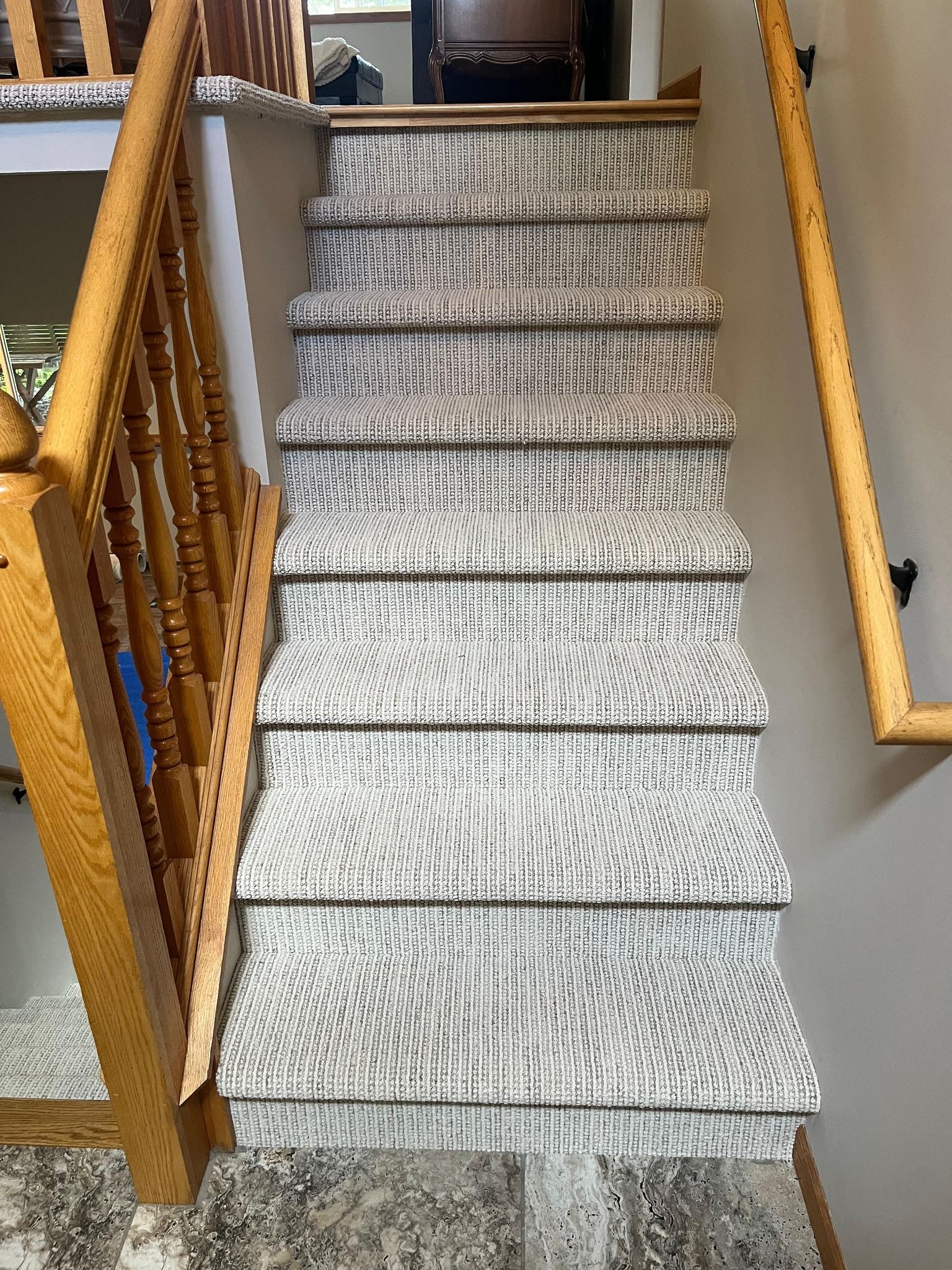 Light gray textured carpet installed on staircase with bound edges and wooden handrail.