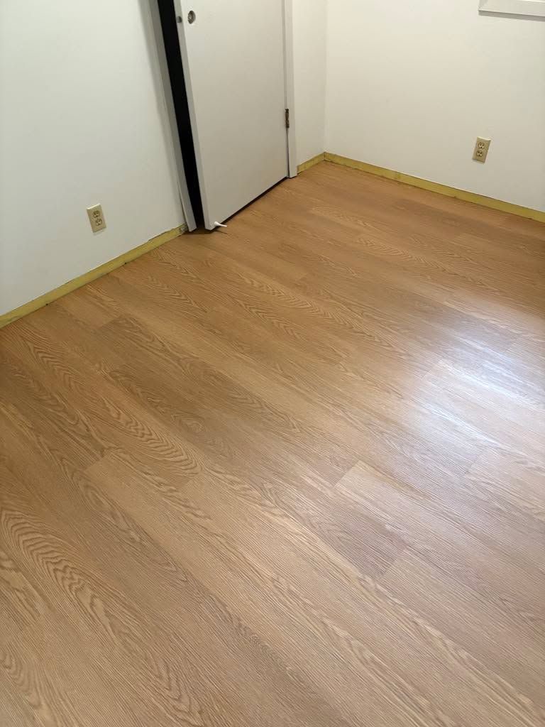 Newly installed light tan wood-grain LVP flooring in a bedroom with white walls and baseboard trim.