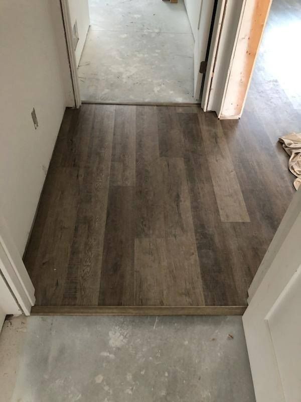 Dark brown luxury vinyl plank flooring installed in entryway transitioning to concrete subfloor.