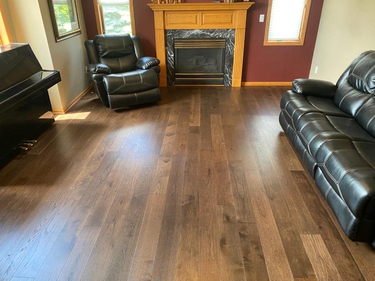 Living room with medium brown engineered hardwood plank flooring, fireplace with wood mantel, and black leather furniture.