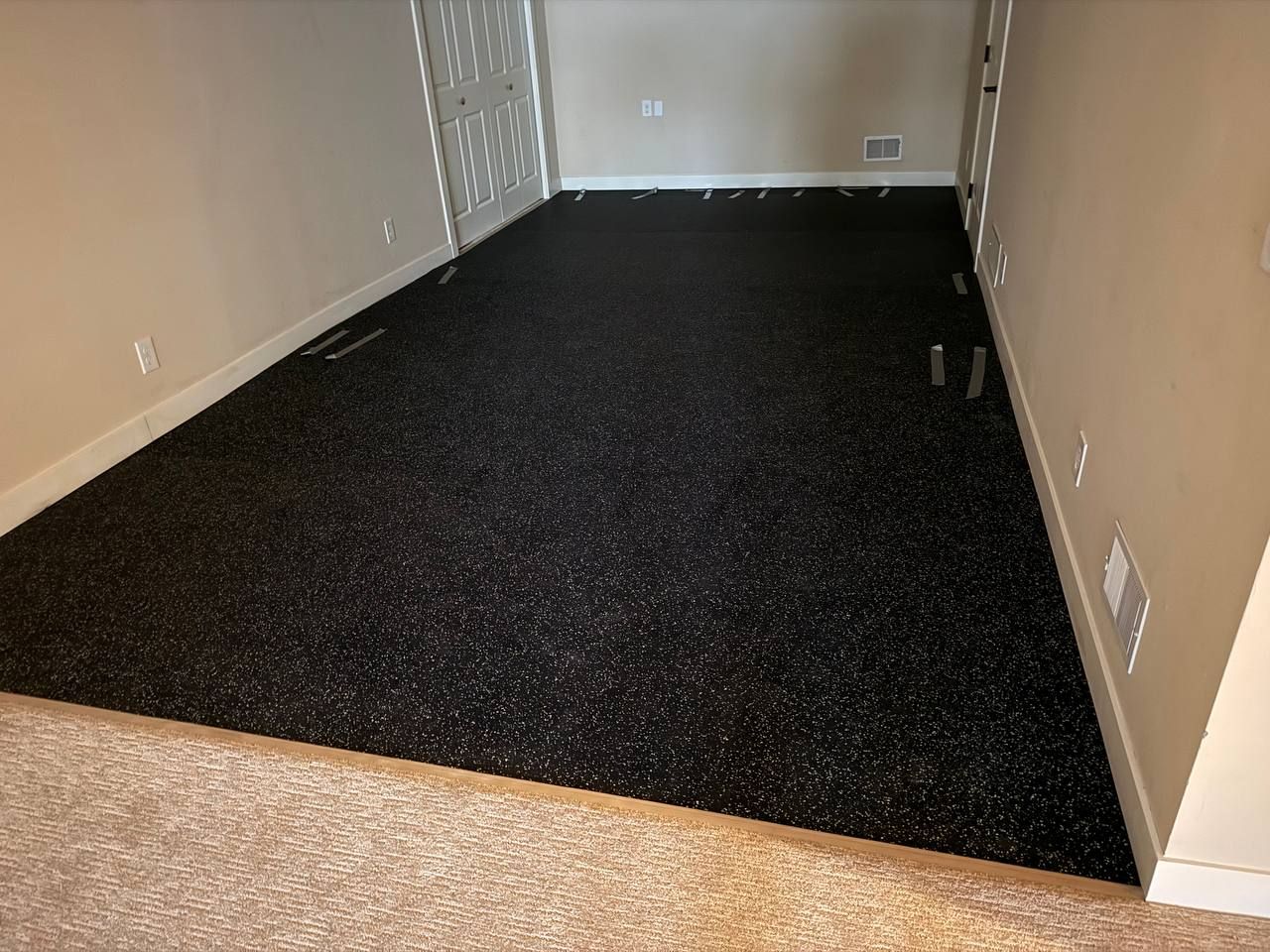 Black luxury vinyl plank flooring installed in a basement room with tan wood-look flooring visible at the entry.