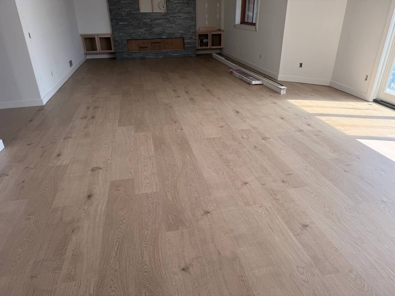 Light tan plank LVP flooring installed in a living room with a stone fireplace wall.