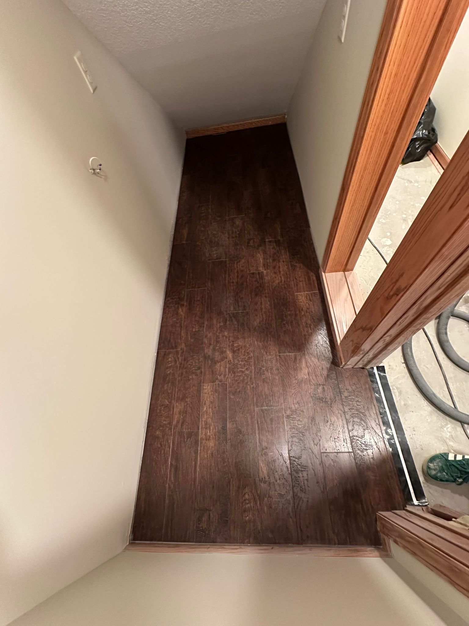 Dark brown plank LVP flooring installed in a hallway with white walls and wood door frame.