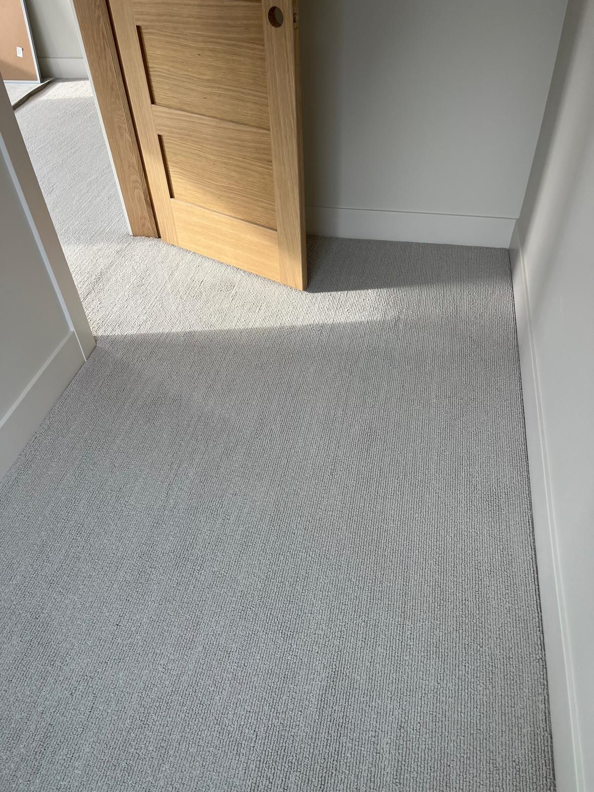 Gray textured carpet installed in a hallway with white walls and a wood closet door.
