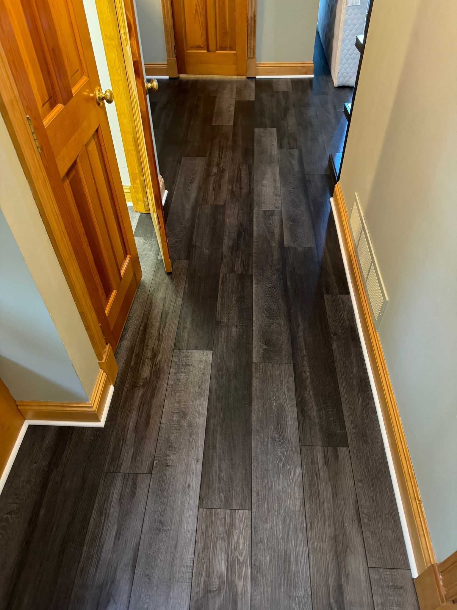 Dark gray wood-look tile planks installed in a hallway with orange wooden doors on both sides.