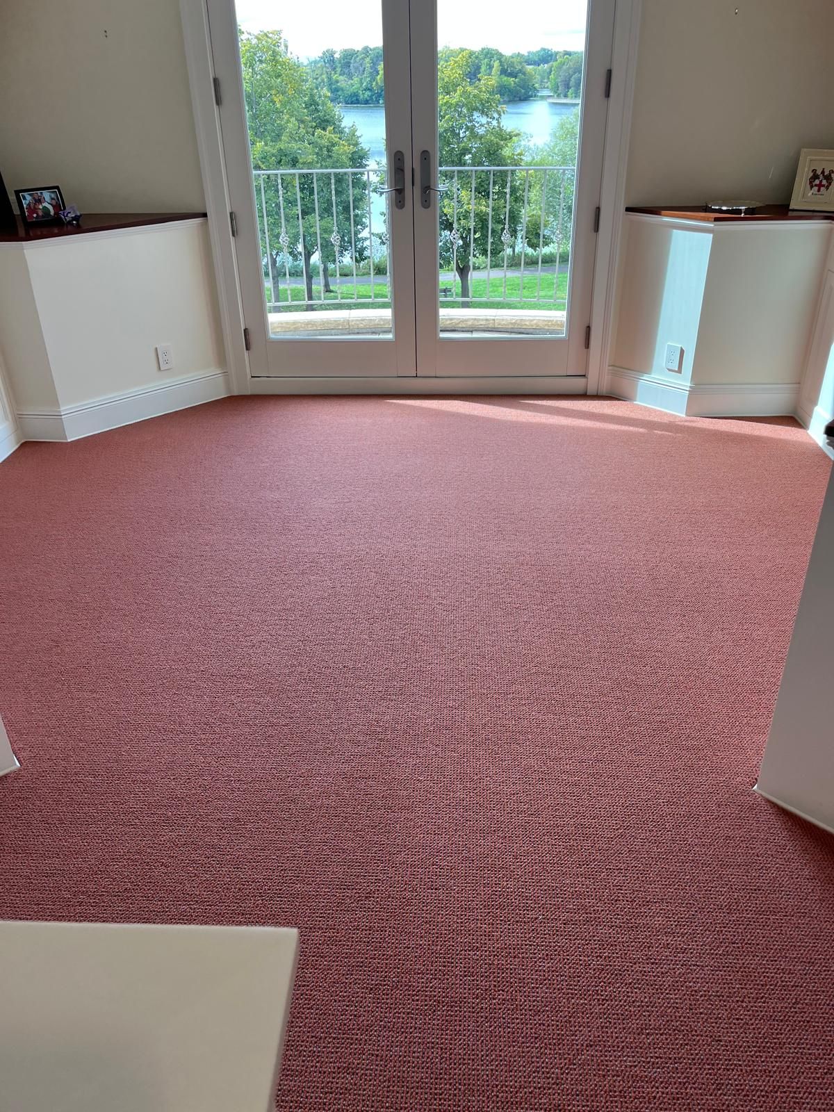 Burgundy carpet installed in a living room with cream walls and French doors overlooking a lake.