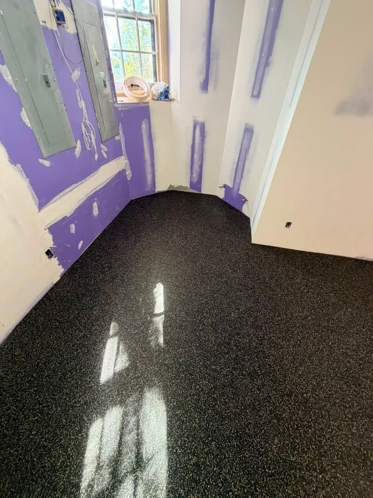 Dark speckled rubber flooring installed in a bathroom under construction with drywall preparation visible on walls.