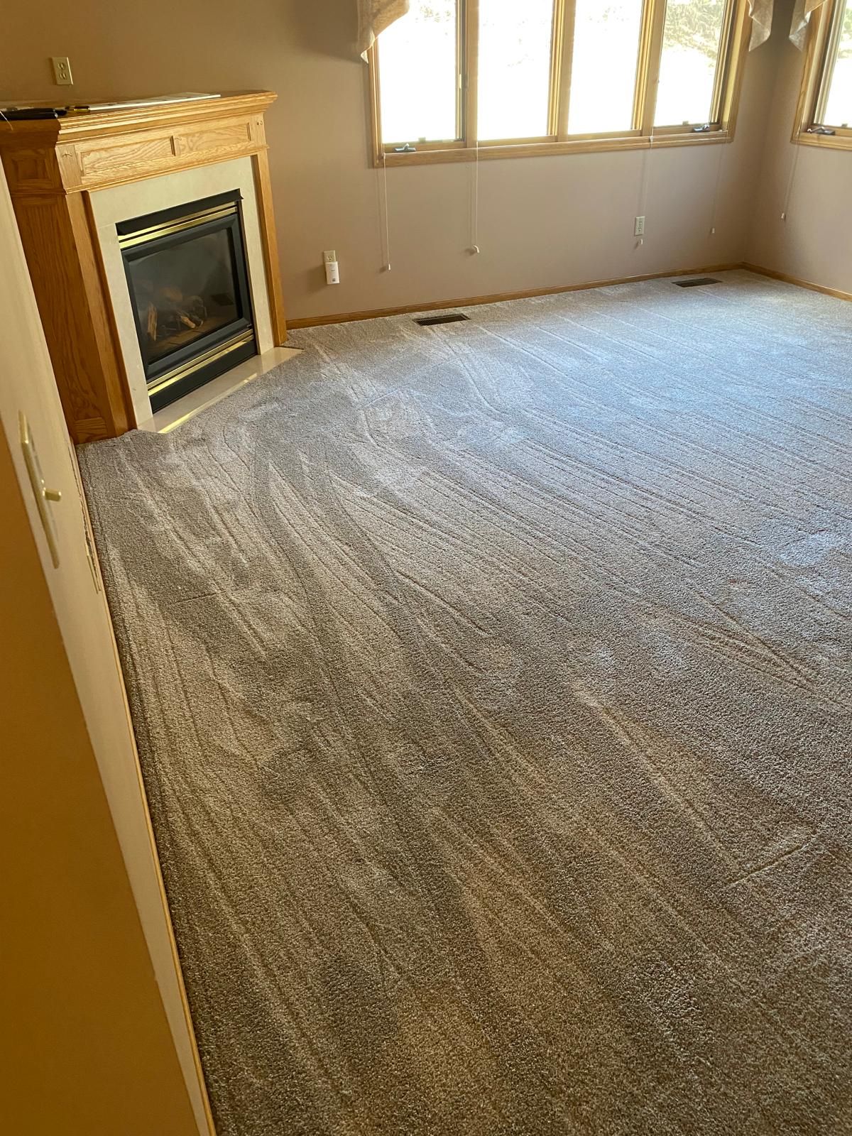 Gray carpet installed in a living room with a fireplace and large windows.