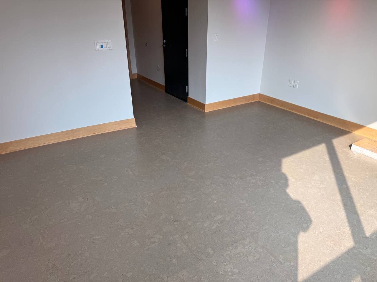 Gray LVP flooring with wood trim installed in a living space with concrete subfloor showing through.