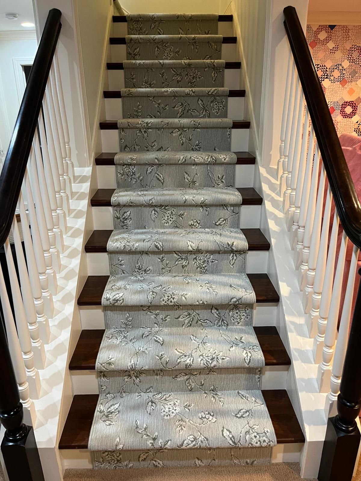 Carpet runner with floral pattern installed on staircase with dark wood treads and white railings.