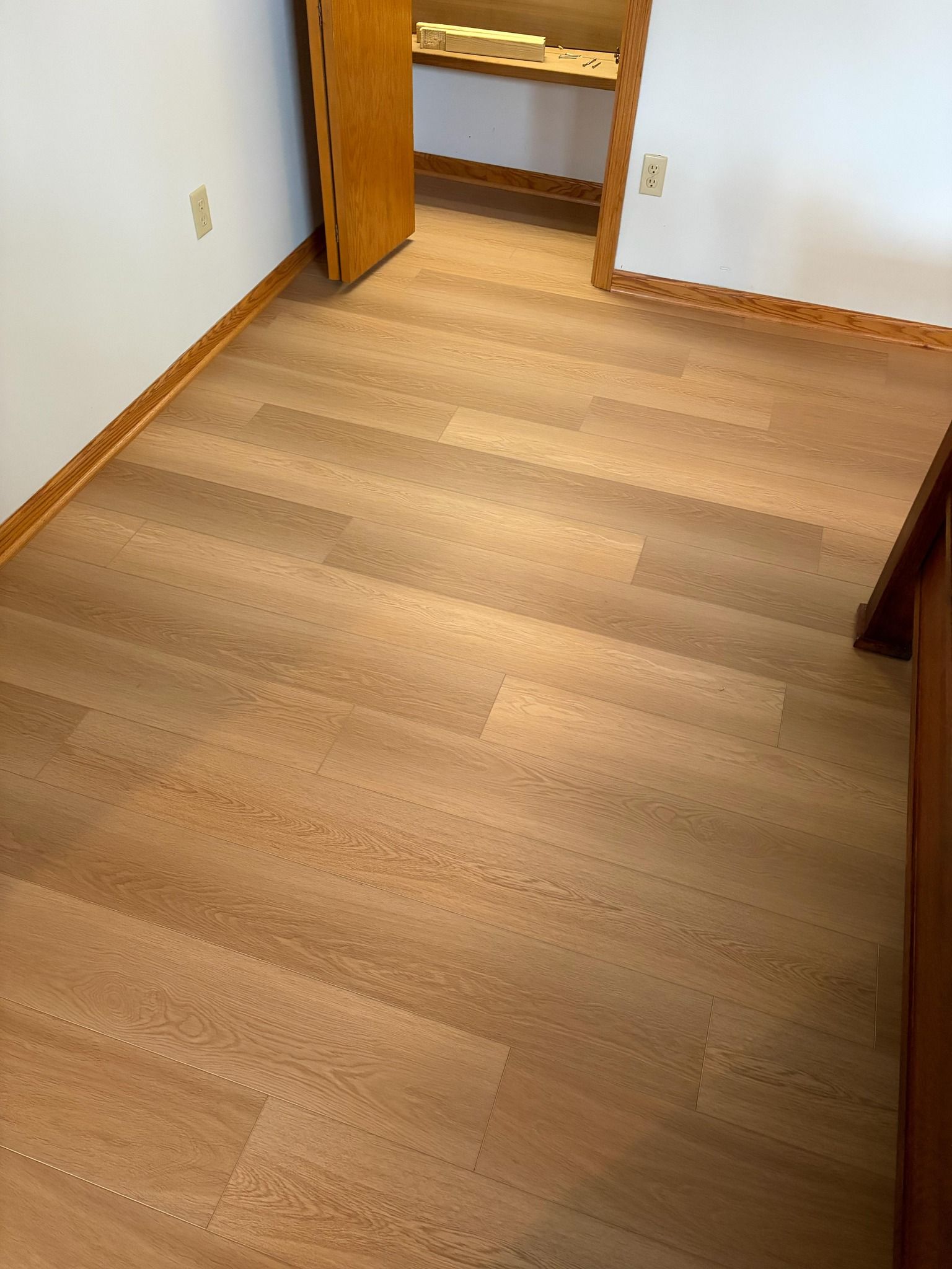 Light tan planks laid in floating installation in a bedroom with wooden closet doors and white walls.