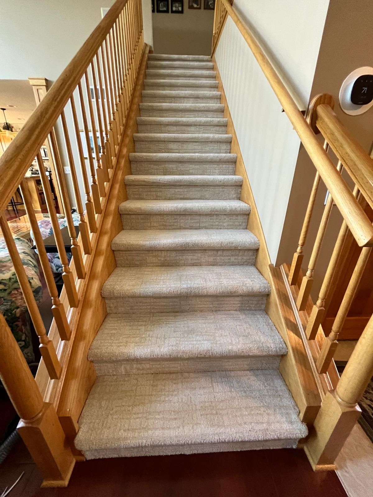 Staircase with tan and gray carpet and natural wood railings and handrails.